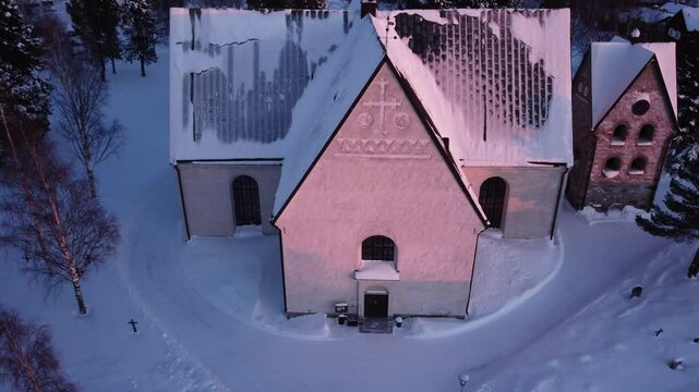 Aerial view, slowly flying next to a church covered in snow during the sunset