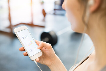 Young fitness girl checking her performance on smatphone after hard workout in gym.