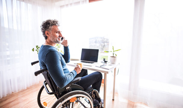 Handsome man in wheelchair working from home office, making phone call. Telecommuting and home office.