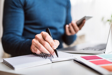 Fototapeta premium Close up of man writing notes in planner, working at desk from home. Telecommuting and home office.
