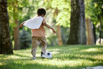 Back view shot of unrecognizable boy kicking ball in green park
