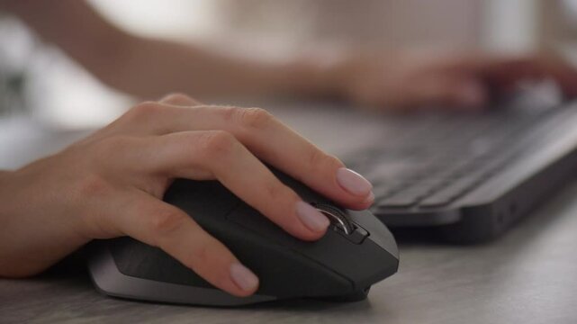 Close-up of hand using a computer mouse while typing on a keyboard