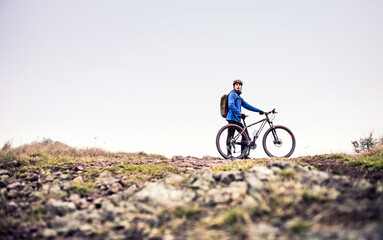 Young man resting by bike in the middle of beautiful nature, early autumn morning. Concept of healthy lifestyle.