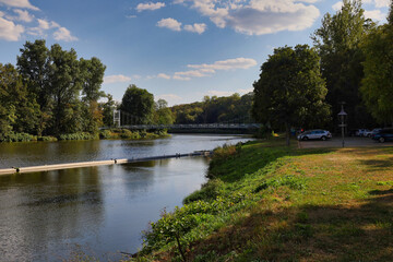 Fototapeta premium Blick über die Mulde auf die historische Hängebrücke und das bewaldete Ufer im Muldental bei sommerlichem Wetter, Grimma, Sachsen, Deutschland