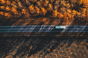 Aerial shot of shuttle bus vehicle driving along the road through wooded landscape in autumn, drone pov