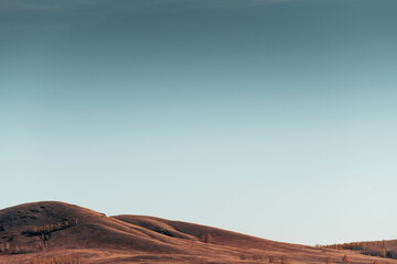 Autumn hills with dry yellow grass and the blue sky at sunset.