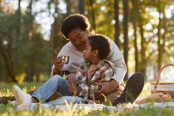 Fototapeta premium African American grandmother and grandson sitting on blanket, chatting and drinking hot tea