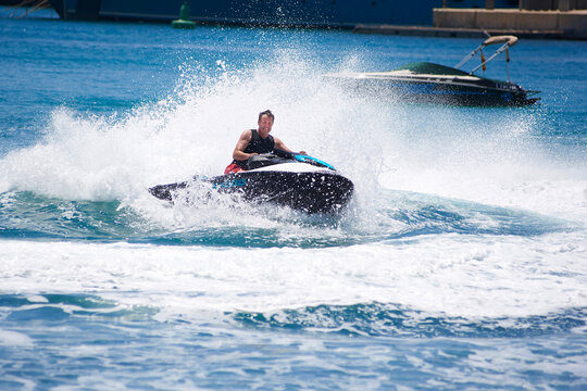 A person riding a jet ski at full speed on the sea in Mallorca, Spain creating splashes and waves.