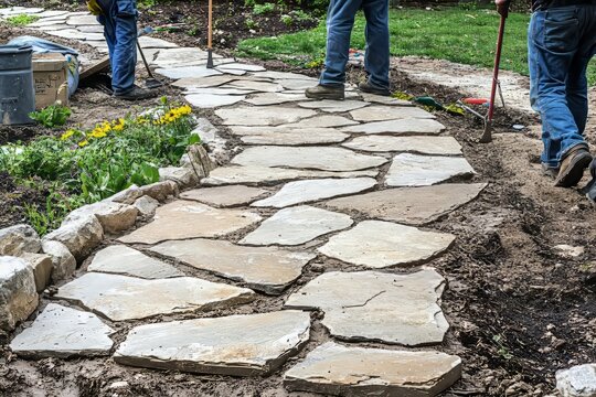 A team of landscapers installing a stone walkway in a residential garden. They&rsquo;re carefully placing each, Generative AI