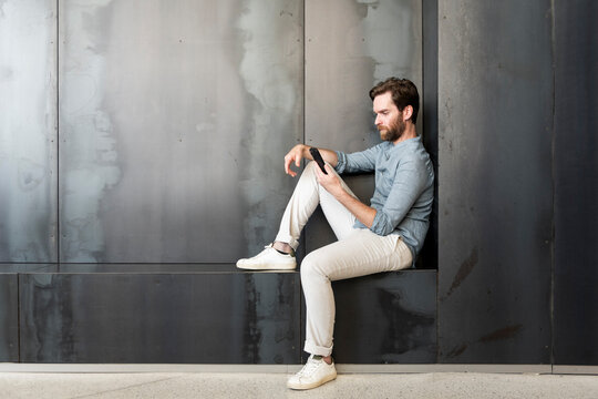 Businessman using smart phone and leaning on wall at office lobby
