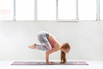 Young woman practicing Bakasana pose on yoga mat at studio