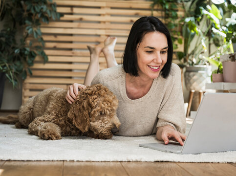 Smiling woman lying near dog and working at home