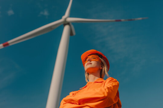Thoughtful engineer wearing protective eyewear and standing near wind turbine