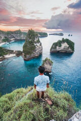 A man stands at the top of a cliff while watching the sunset in the background. © Balnyes Visuals