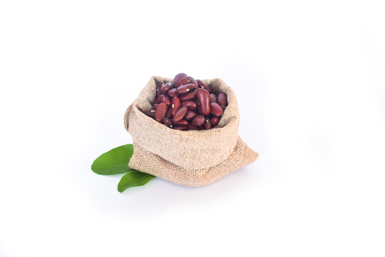 A jute bag filled with organic Almond kernels (Prunus dulcis) is placed over a pile of Almonds, isolated on a white background. 