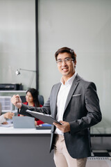 Young attractive Asian male office worker business suits smiling at camera in office .