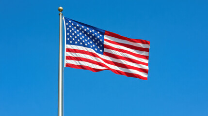 Fototapeta premium American flag waving against a clear blue sky, symbolizing pride, freedom, and patriotism in the United States.