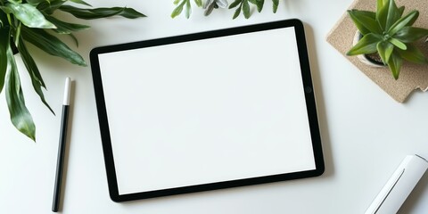 A tablet, pen, and plants on a white desk.