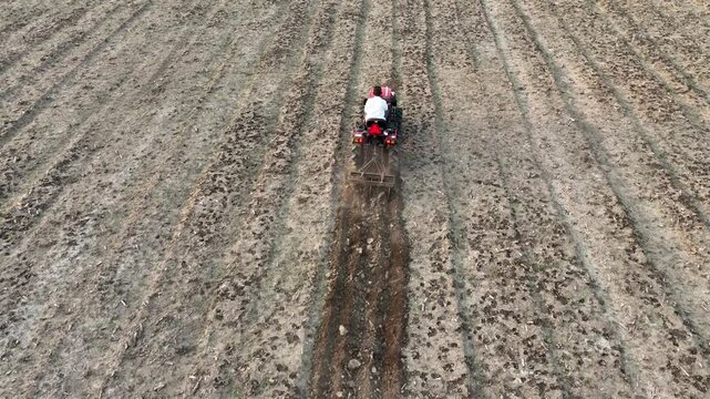 aerial drone shot of farmer working ploughing plowing in the brown open farm land with red tractor organic farming in desert wild dry area land soil with machinery equipment
