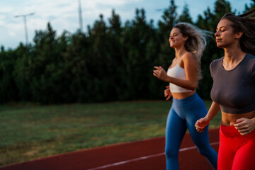 Two young women jogging on a track, smiling and enjoying their workout. They are wearing athletic outfits.