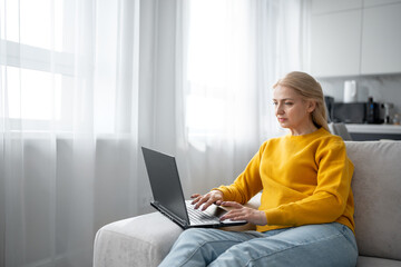 Naklejka premium A blonde woman is working with intense focus from her home office, typing on a laptop