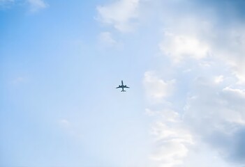 Fototapeta premium Airplane flying high in a clear blue sky with fluffy white clouds.