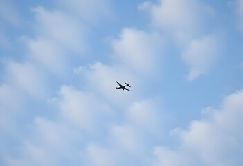 Obraz premium Airplane flying high in a clear blue sky with fluffy white clouds.