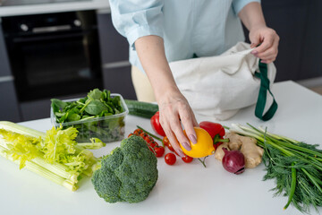 In a contemporary kitchen, a woman is unloading fresh groceries using ecofriendly bags
