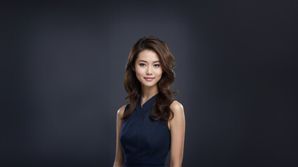 A beautiful brunette Japanese businesswoman with neat hair and healthy skin smiles at the camera. She has natural makeup and is posing in a studio