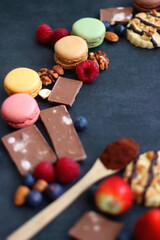 Macarons, chocolate, cookies, berries and various nuts on dark blue background. Selective focus.