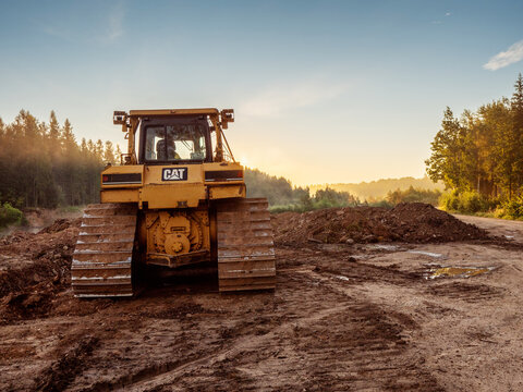 Ogre area, Latvia - 07.15.2024: Massive powerful CAT bulldozer in rural forest area. Construction and development job. Heavy machinery at work. Sunrise time. Nobody.