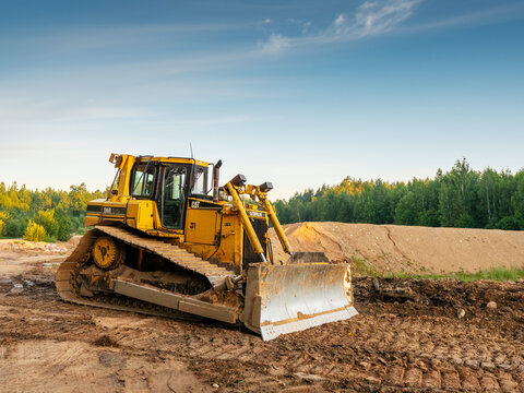 Ogre area, Latvia - 07.15.2024: Massive powerful CAT bulldozer in rural forest area. Construction and development job. Heavy machinery at work. Sunrise time. Nobody.