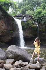 girl in yellow dress Standing and taking photos of the waterfall