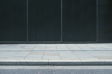 A minimalist photograph showing an empty sidewalk in front of a dark building wall, highlighting simplicity and the beauty of clean, uncluttered urban design.
