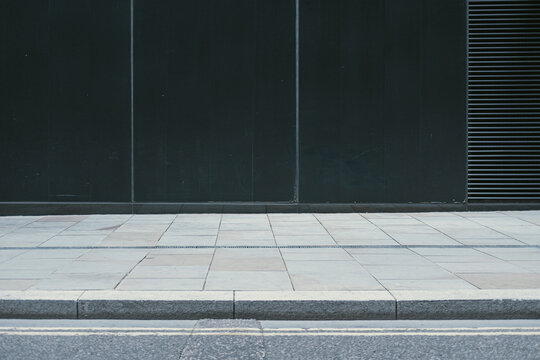 A minimalist photograph showing an empty sidewalk in front of a dark building wall, highlighting simplicity and the beauty of clean, uncluttered urban design.
