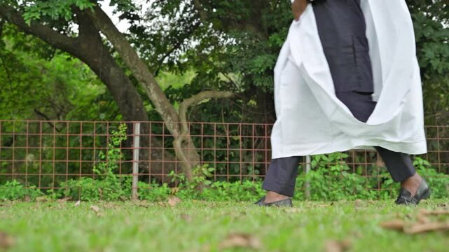 Slow motion 4k resolution of the legs of an African male in a black and white flowing traditional babariga attire walking outdoor in a green garden depicting power, confidence, purpose and focus.