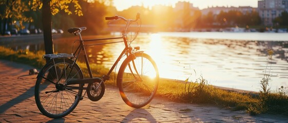 A vintage bicycle resting on the lakeside path under the warm glow of a setting sun, with a scenic cityscape in the background.