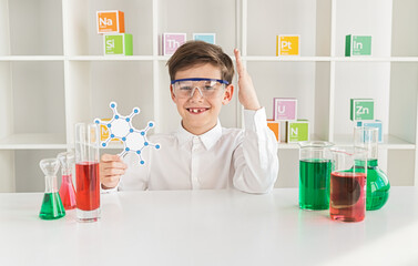 Smiling young boy wearing safety goggles in a chemistry lab, holding a molecule model. Laboratory equipment and colorful chemical solutions surround him.