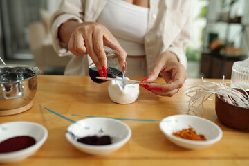 Close-up of woman adding colored dye to the wax while making handmade candles