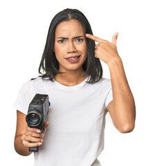 Latina with vintage camera, filming showing a disappointment gesture with forefinger.