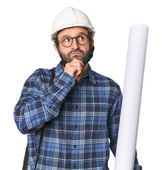 Hispanic male architect with plans looking sideways with doubtful and skeptical expression.