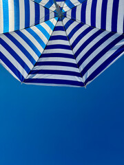 Fragment of white and blue striped beach umbrella close up against clear blue sky with text space