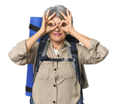 Caucasian mid-age female with hiking gear showing okay sign over eyes