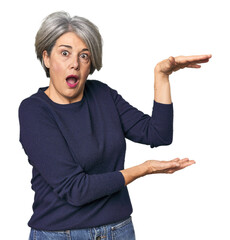 Caucasian mid-age female on studio background shocked and amazed holding a copy space between hands.