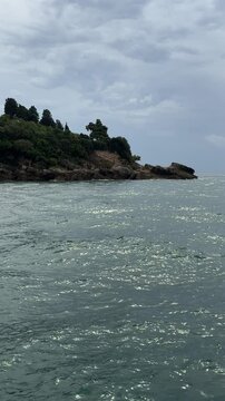 Blue shiny sea waves and rocky coast, vertical video.