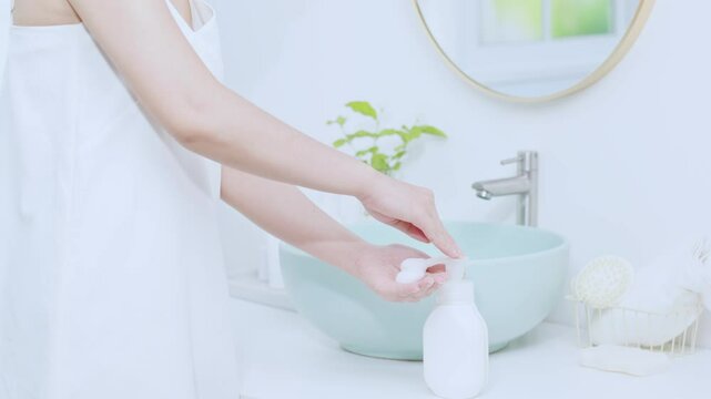 Close-up of a girl taking foam from a white unlabeled product bottle and rubbing her hands together to even out the foam. Set in a bathroom, the shot shows the suds of a cleaning product