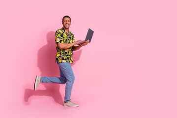 Full body photo of attractive young man running hold netbook dressed stylish tropical print clothes isolated on pink color background