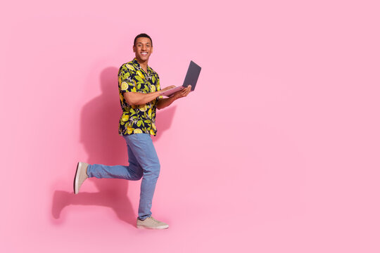 Full body photo of attractive young man running hold netbook dressed stylish tropical print clothes isolated on pink color background