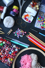 Colorful beads, coloring pencils, glitter, needles, string, hoop, tape and scissors on dark background. Various colorful craft supplies. Flat lay.