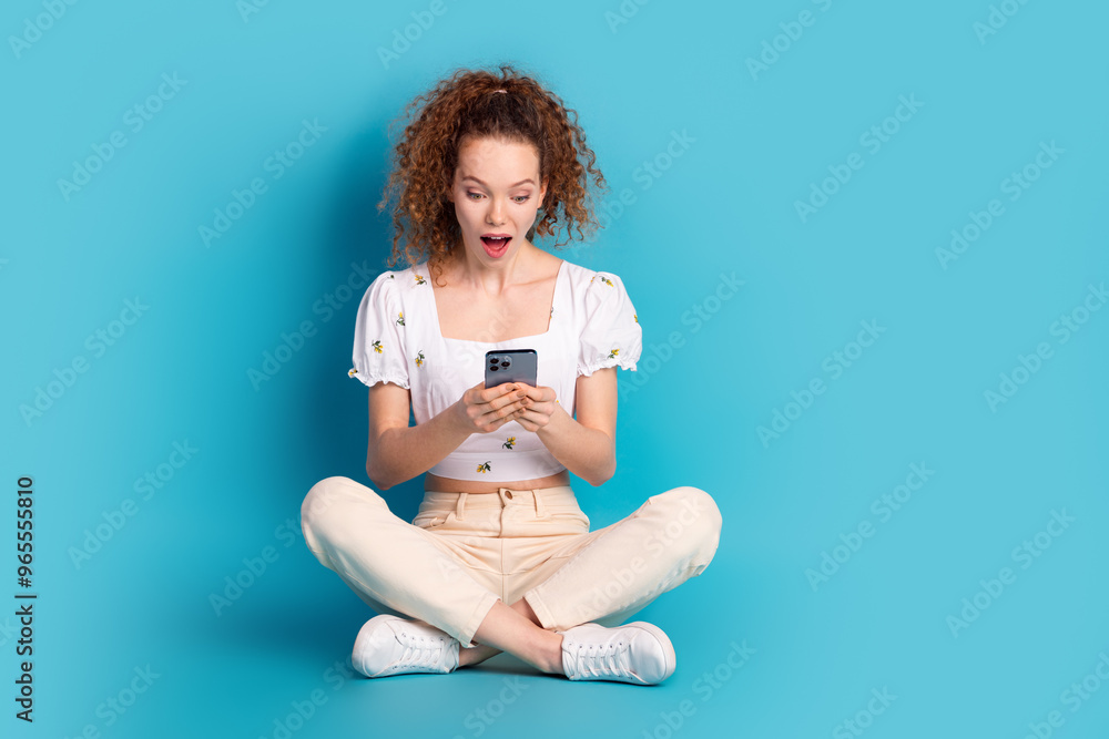 Poster Full body photo of attractive young woman sit floor hold device amazed dressed stylish white clothes isolated on blue color background